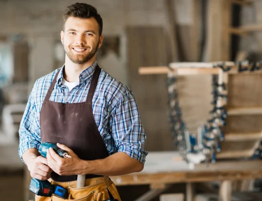 Ein Handwerker in einer Werkstatt, der einen Schraubendreher hält und lächelt