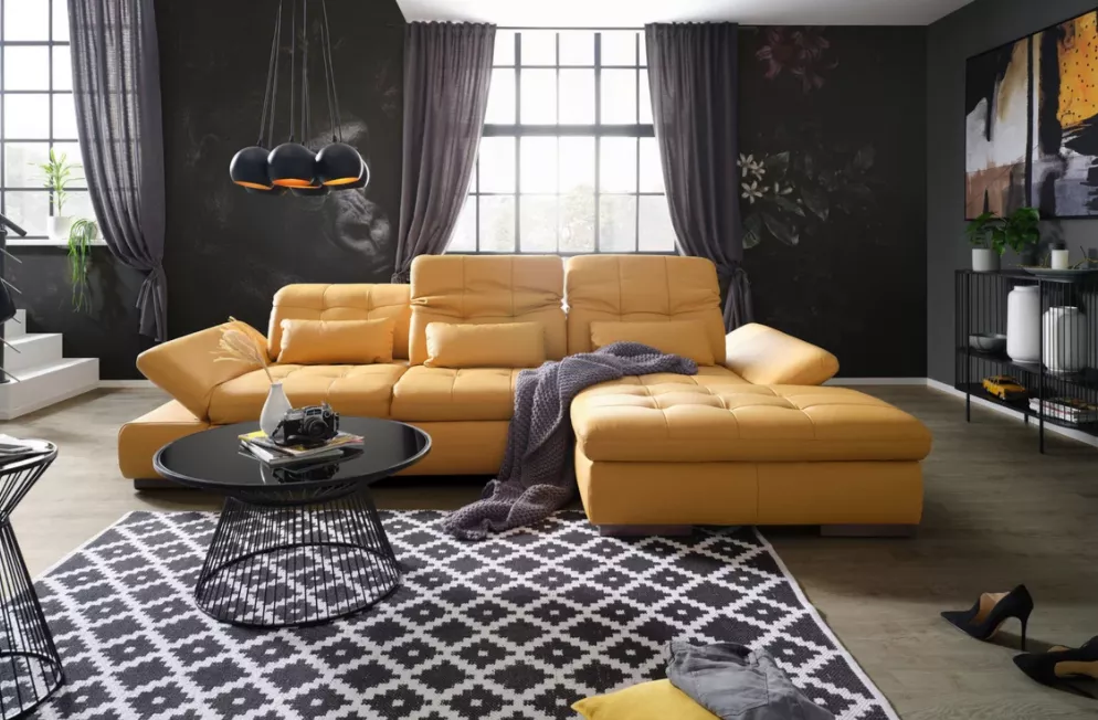 Wohnzimmer Trends 2025 – modernes Interieur mit gelbem Designersofa, schwarzem Hochglanz-Couchtisch, dunkler Wandgestaltung und großem Fenster.
