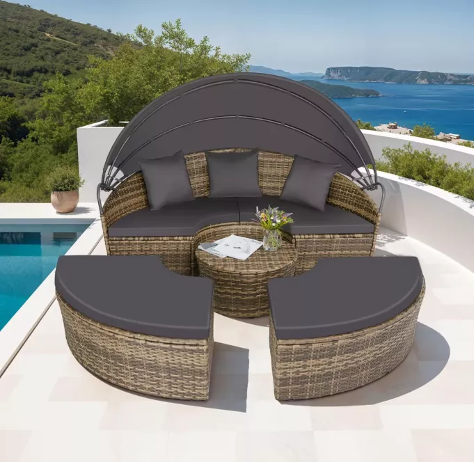 Garten gestalten mit halbrunder Rattan-Lounge, grauen Polstern, kleinem Tisch, Sonnendach und Ausblick auf Pool, Natur und Meer.