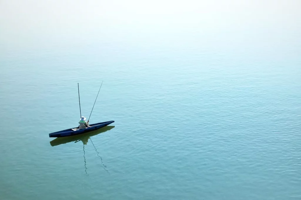 Eine einzelne Person sitzt in einem schmalen Boot auf ruhigem Wasser und angelt – Symbol für Einfachheit, Ruhe und minimalistische Lebensweise.