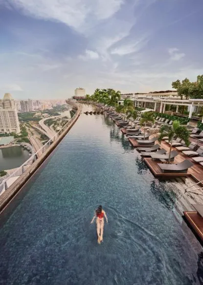 Rooftop-Infinity-Pool im Marina Bay Sands in Singapur mit Skyline und Liegeterrassen, Person schwimmt im Vordergrund