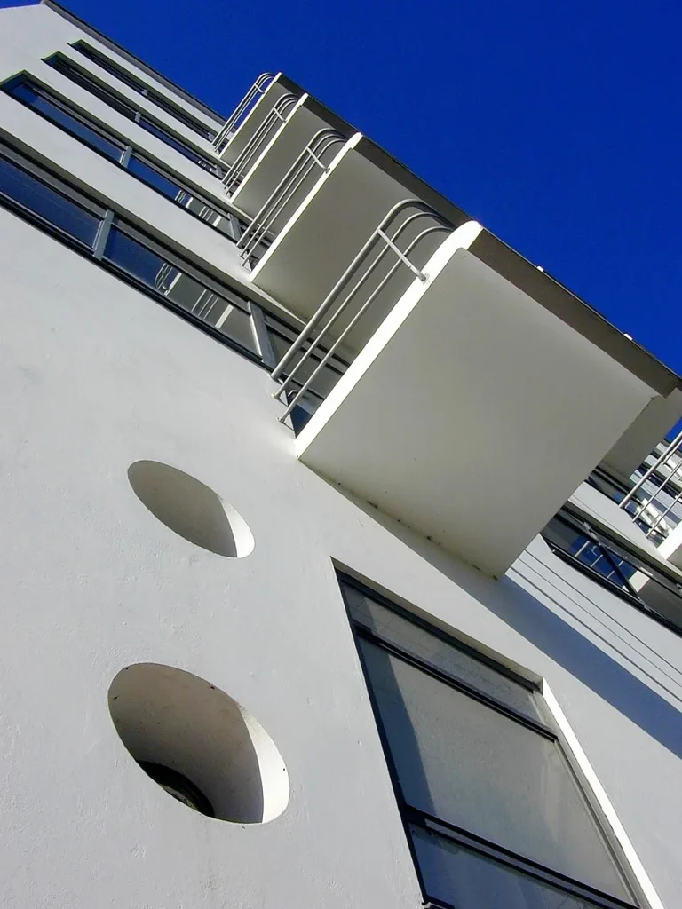 Bauhaus Stil Architektur mit weißen Balkonen, filigranen Stahlgeländern, Fensterbändern und runden Bullaugen in extremer Aufsicht vor blauem Himmel