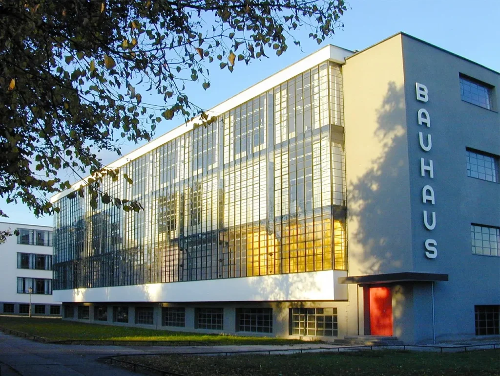 Bauhaus Stil Architektur: Bauhausgebäude in Dessau mit Glasvorhangfassade, klaren Kuben und roter Eingangstür im Abendlicht