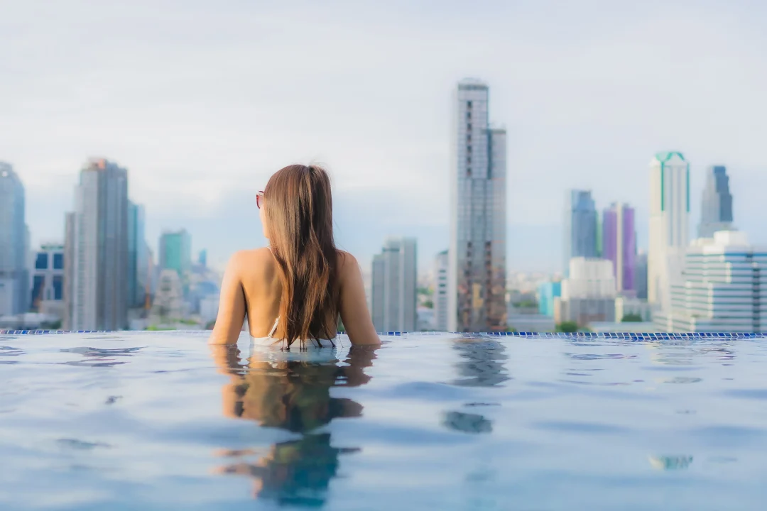 Frau entspannt in einem Rooftop-Infinity-Pools mit Blick auf die Skyline einer Großstadt