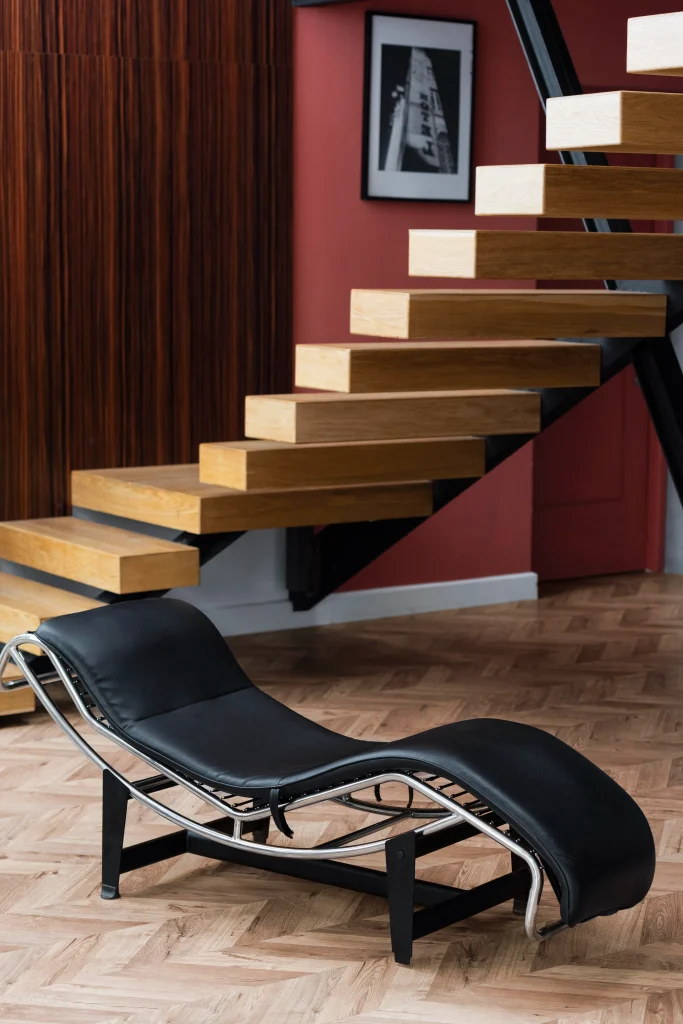 Bauhaus Stil Möbel: schwarze Chaiselongue mit Stahlrohrgestell vor schwebender Holztreppe in modernem Wohnraum