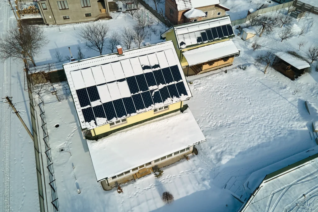 Balkonkraftwerk im Winter auf Hausdach mit Schnee und teilfreigelegten Solarmodulen