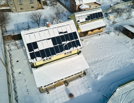 Balkonkraftwerk im Winter auf Hausdach mit Schnee und teilfreigelegten Solarmodulen