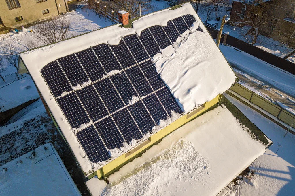 Balkonkraftwerk im Winter mit teilweise schneebedeckten Solarmodulen auf Hausdach