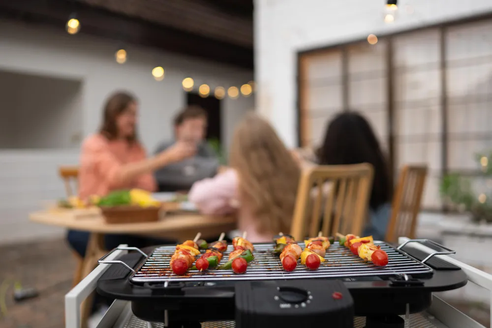 Gemüsespieße und Würstchen auf einem Elektro-Tischgrill beim Grillabend im Garten