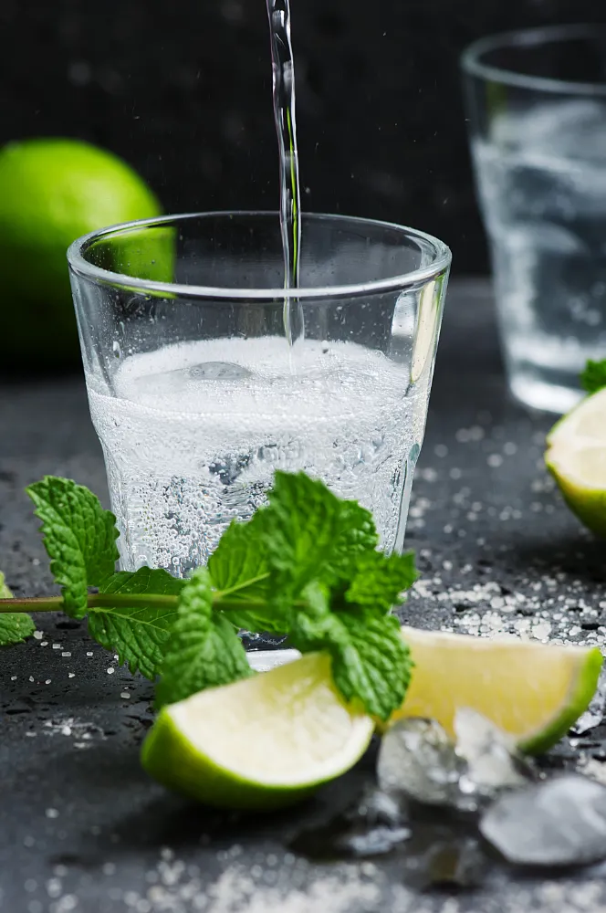 Glas mit sprudelndem Wasser, Limette und frischer Minze auf dunklem Hintergrund