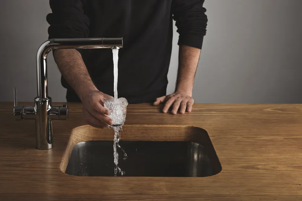 Mann lässt Wasser aus einem Küchenhahn in ein Glas laufen